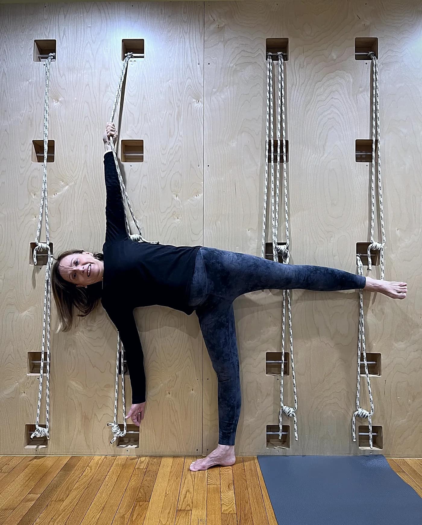 A member holding half-moon pose at the studio’s rope wall, one hand on a rope and the opposite leg extended