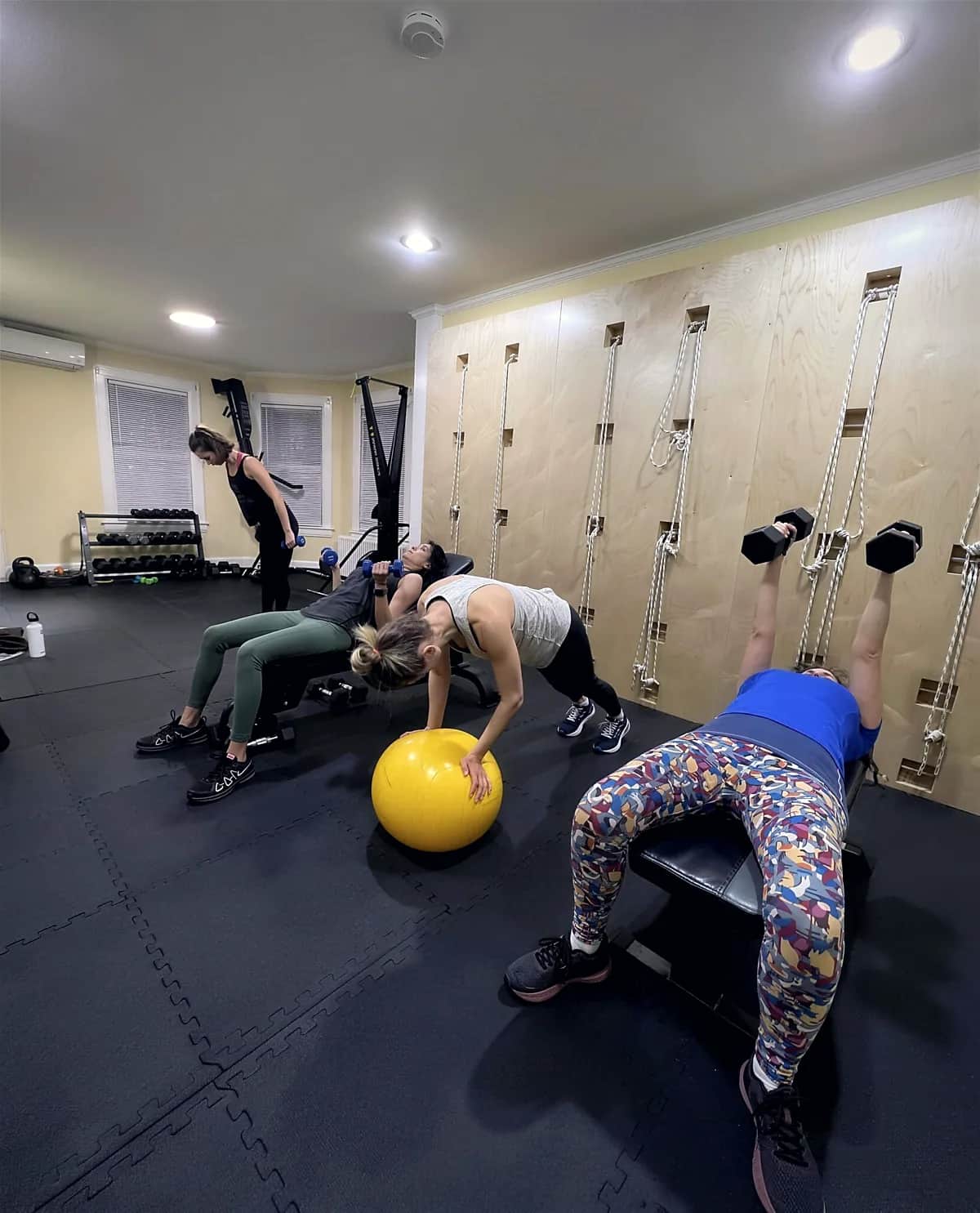 Three members in a small group session working with dumbbells, a bench and a stability ball