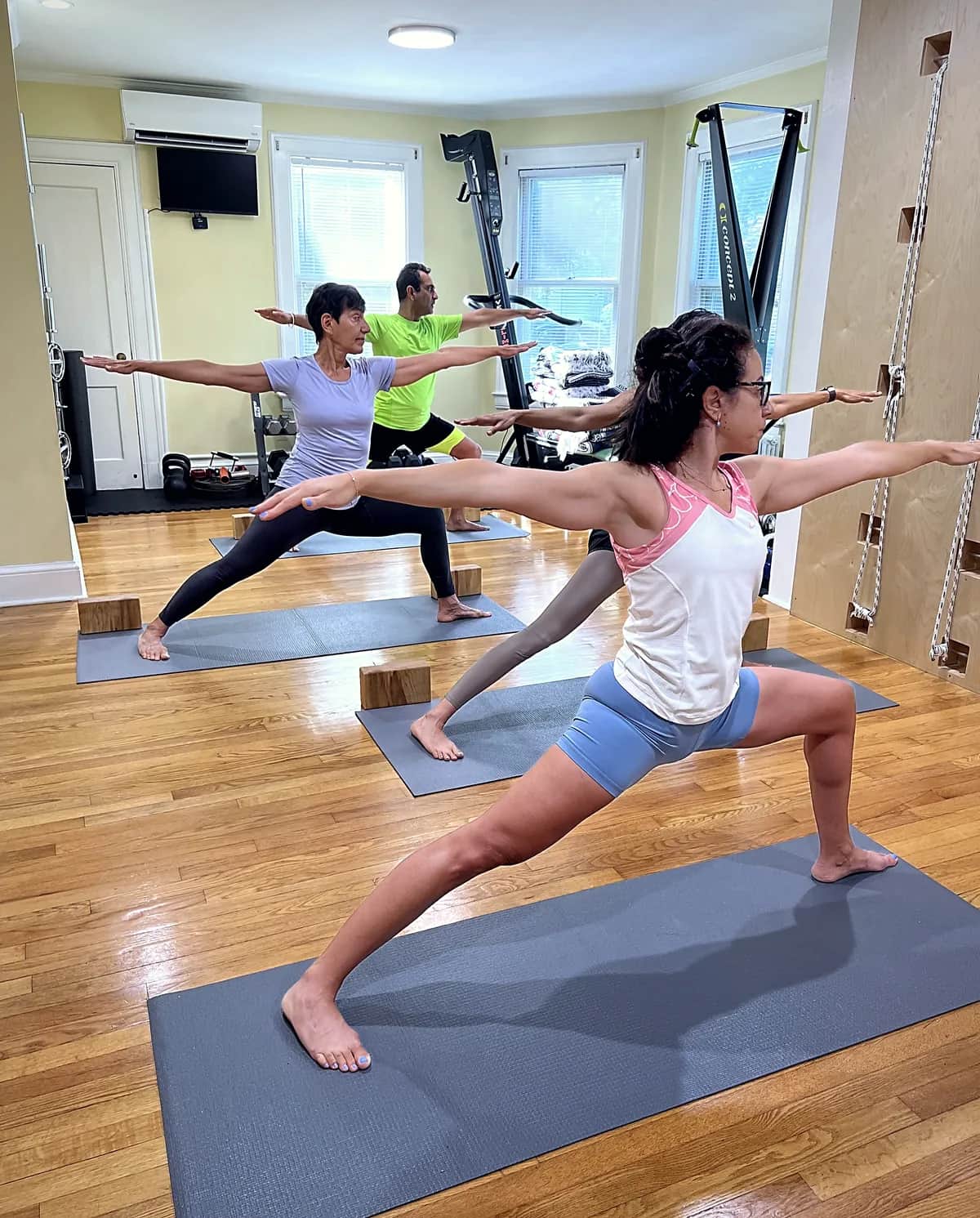 Three members holding Warrior Two on mats across the studio floor, arms extended and gaze forward
